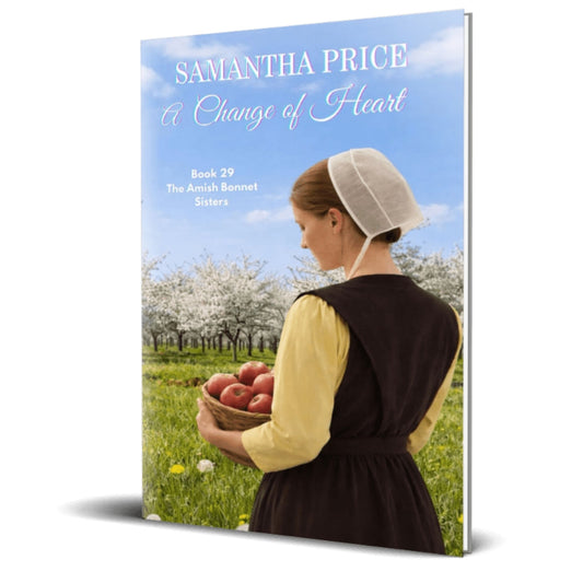 A 3D book cover mockup for 'A Change of Heart' by Samantha Price, Book 29 in 'The Amish Bonnet Sisters' series. The cover features a woman in an Amish bonnet and dress holding a basket of red apples in an apple orchard.